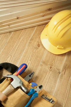 Scène d'intérieur sur plancher en bois massif avec casque de chantier jaune et outils de menuiserie disposés sur parquet naturel