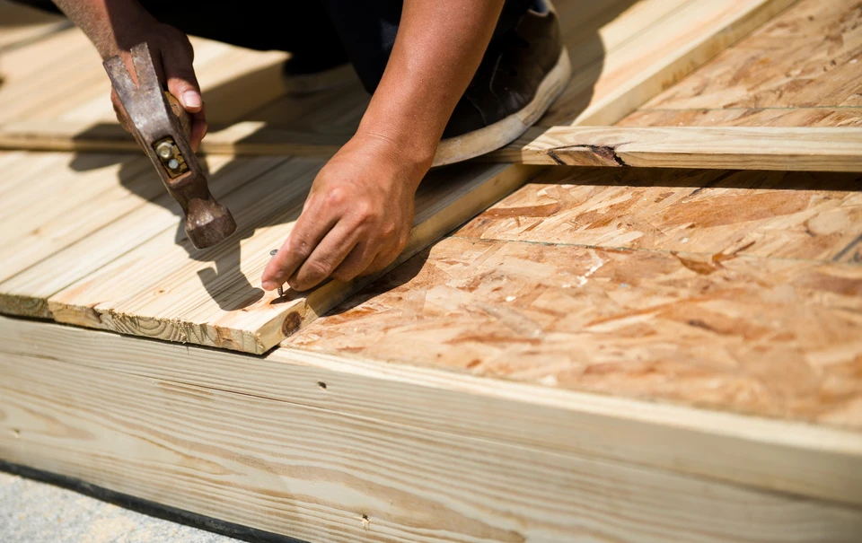 Artisan travaillant en extérieur sur chantier de construction, utilisant un rabot manuel pour façonner une planche en bois