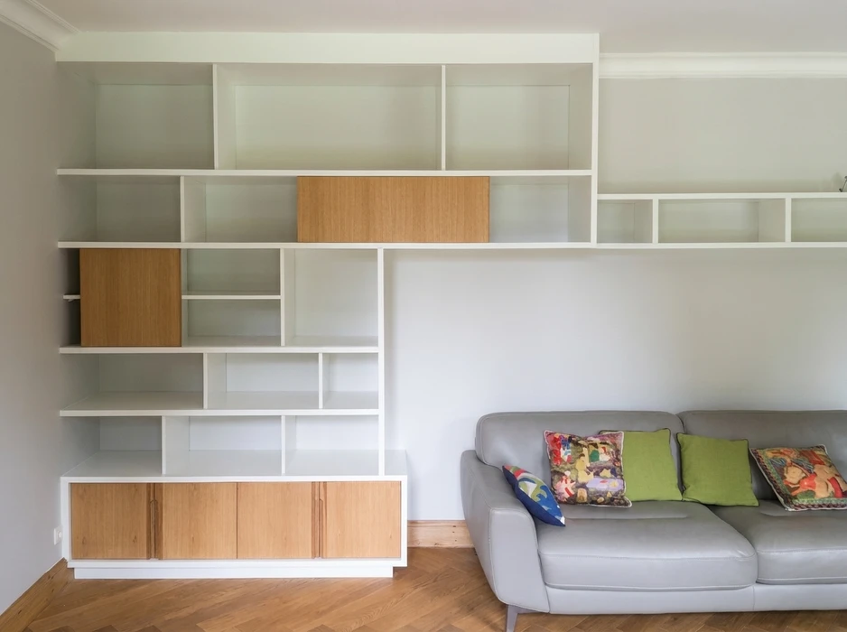 Bibliothèque murale sur mesure en laque blanche, design asymétrique avec niches ouvertes de dimensions variées et portes coulissantes en bois de chêne naturel
