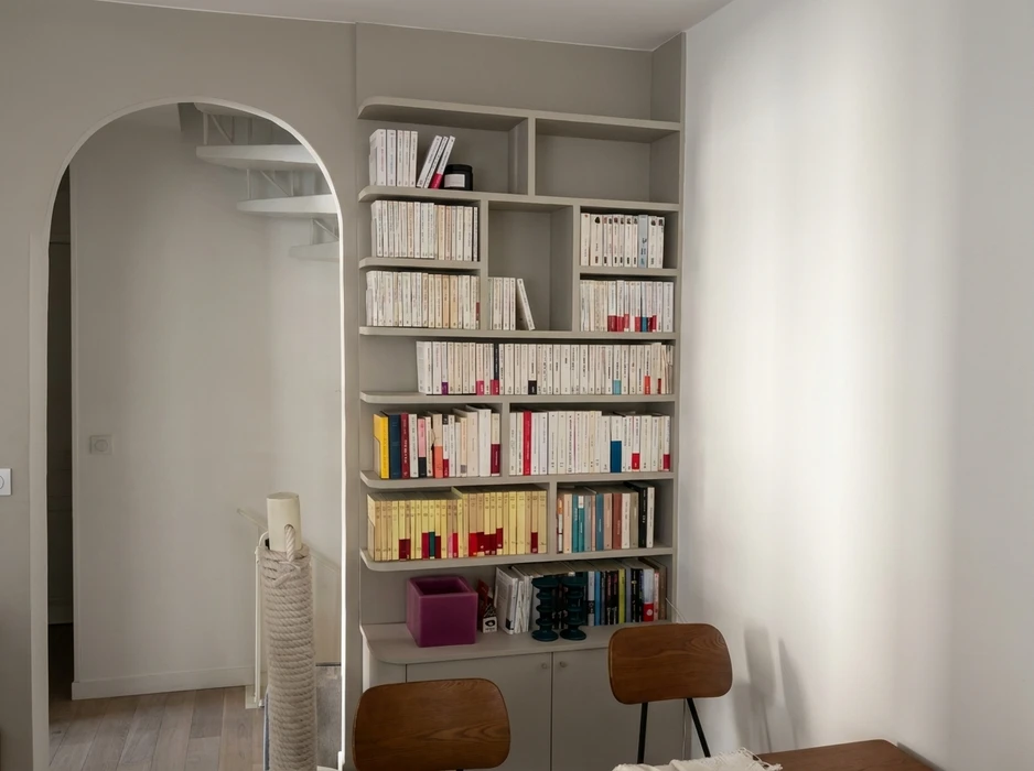 Bibliothèque encastrée sur mesure, teinte gris clair, remplie de livres de poche et ouvrages reliés, organisés par rangées denses
