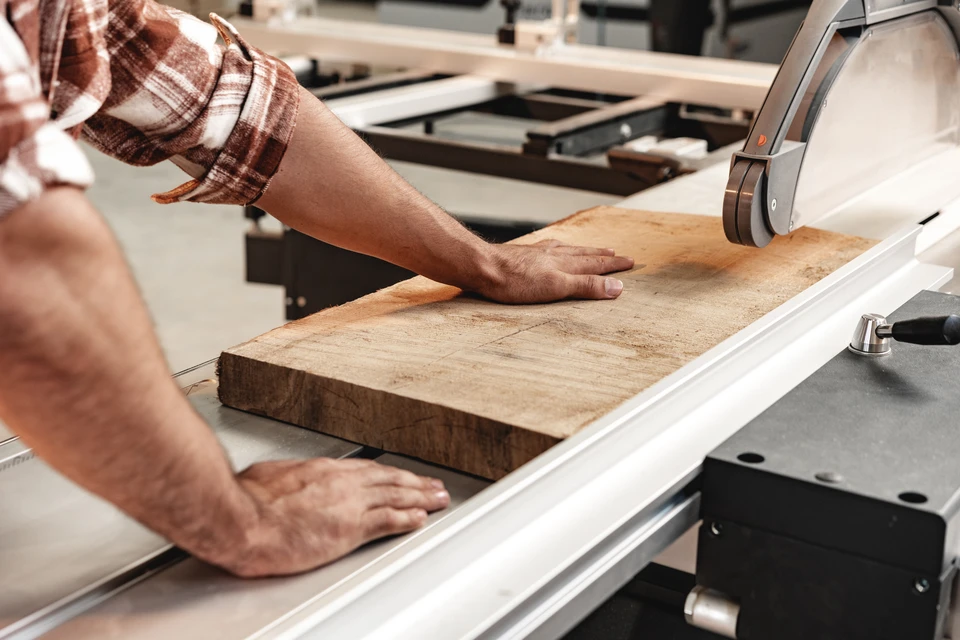 Artisan menuisier travaillant dans son atelier, manipulant une planche de bois massif sur établi