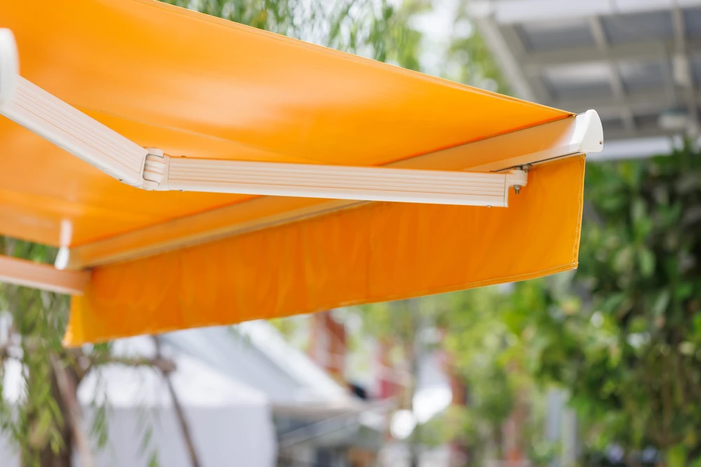 Technicien en tenue bleue installant un store banne rétractable sur la terrasse d'une maison résidentielle