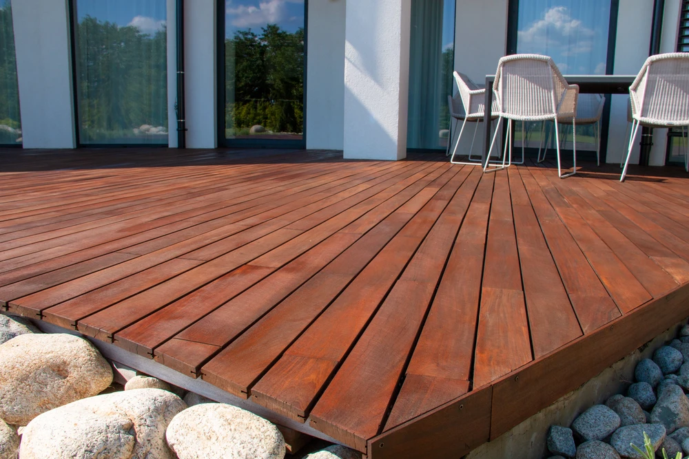 Scène extérieure montrant une terrasse en bois avec planches découpées posées au sol sur un terrain herbeux avec mousse